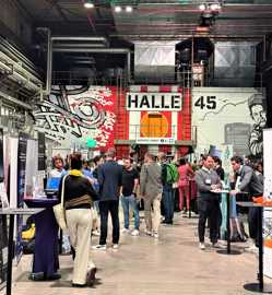 Messebesucher in einer ehemaligen Fabrikhalle vor einer Wand mit Graffiti und der Aufschrift "Halle 45".
